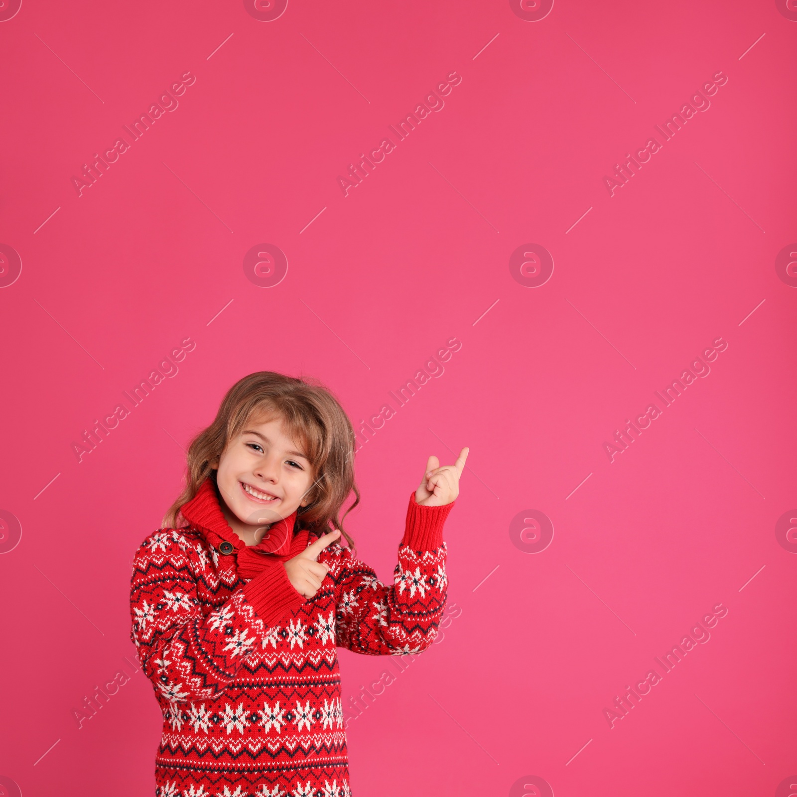 Photo of Cute little girl in red Christmas sweater against pink background. Space for text