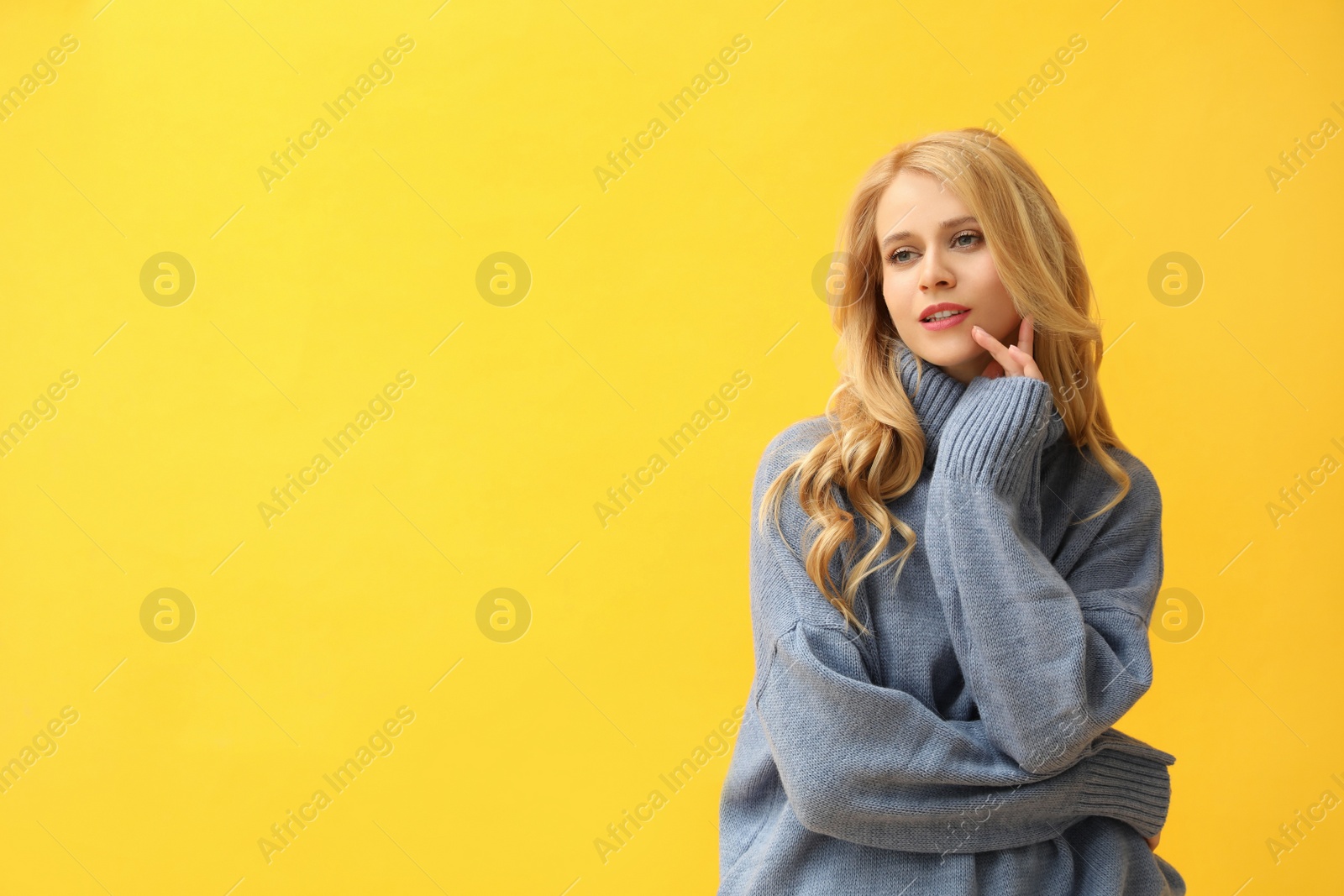 Photo of Beautiful young woman wearing warm blue sweater on yellow background. Space for text