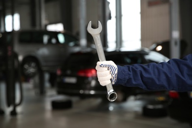 Technician holding wrench in automobile repair shop, closeup