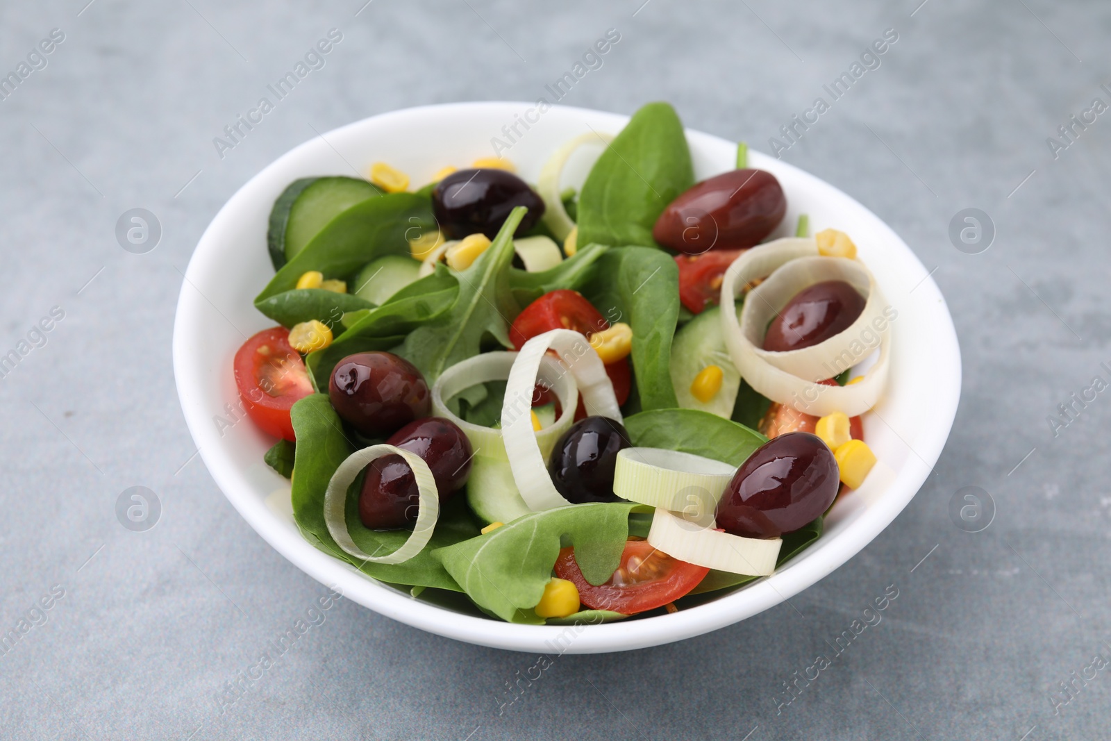 Photo of Bowl of tasty salad with leek and olives on grey table, closeup