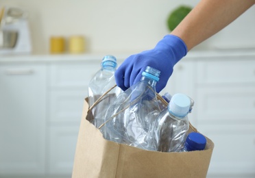 Photo of Woman holding paper bag with used plastic bottles indoors, closeup. Recycling problem