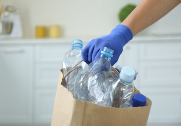 Woman holding paper bag with used plastic bottles indoors, closeup. Recycling problem