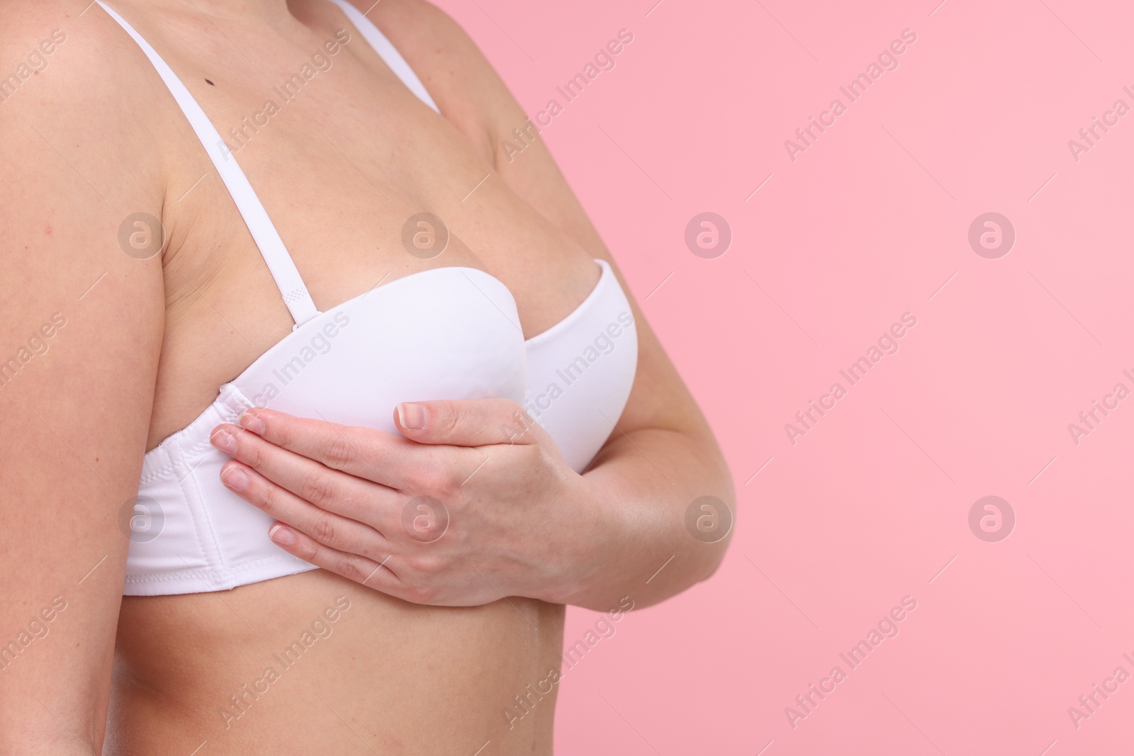 Photo of Mammology. Woman in bra doing breast self-examination on pink background, closeup and space for text