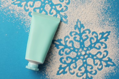 Photo of Tube of hand cream and snowflakes on light blue background, top view. Winter skin care