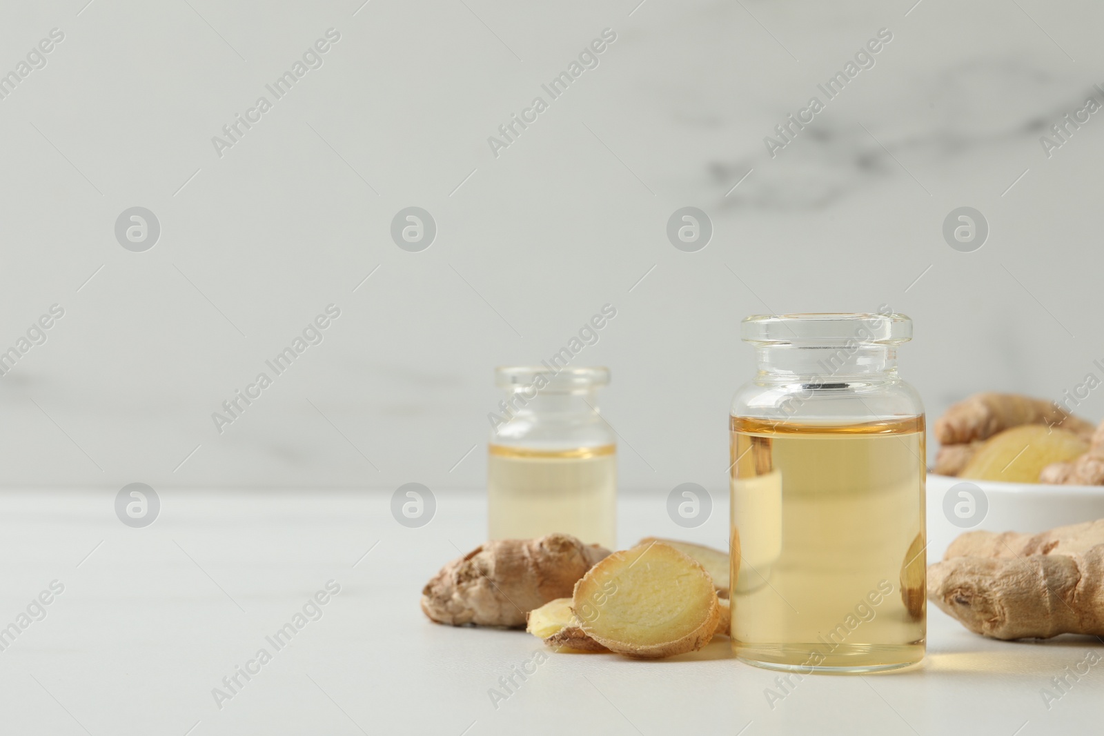 Photo of Glass bottle of essential oil and ginger root on white table, space for text