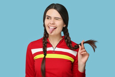 Photo of Happy young woman showing her tongue on light blue background