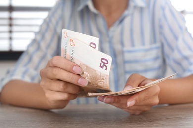 Woman with Euro banknotes at wooden table indoors, closeup
