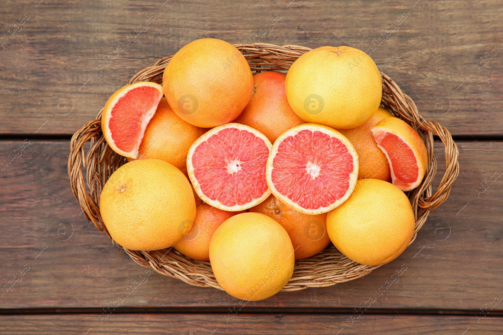 Photo of Wicker basket with fresh grapefruits on wooden table, top view