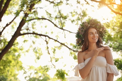 Young woman wearing wreath made of beautiful flowers outdoors on sunny day