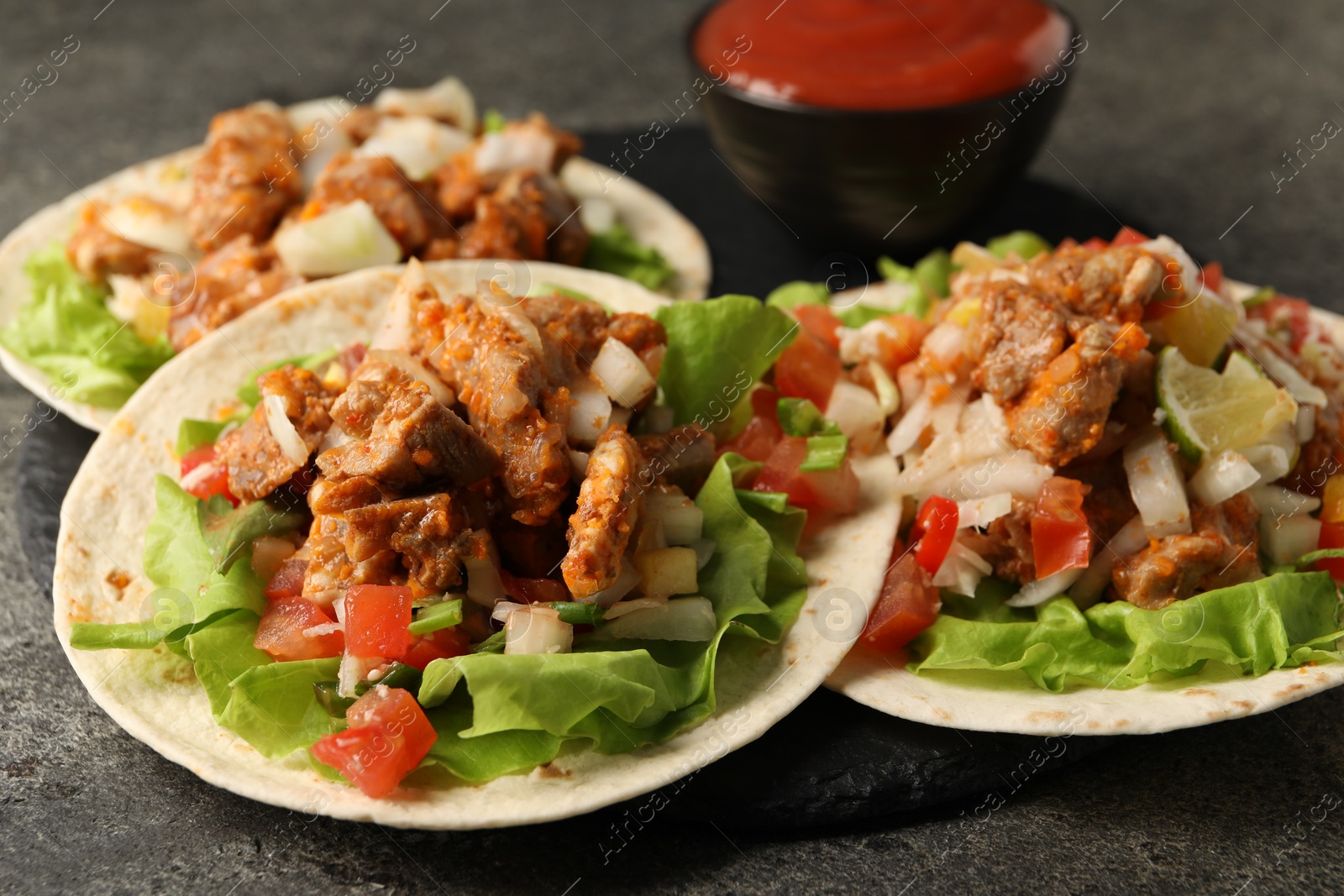 Photo of Delicious tacos with vegetables and meat on grey textured table, closeup