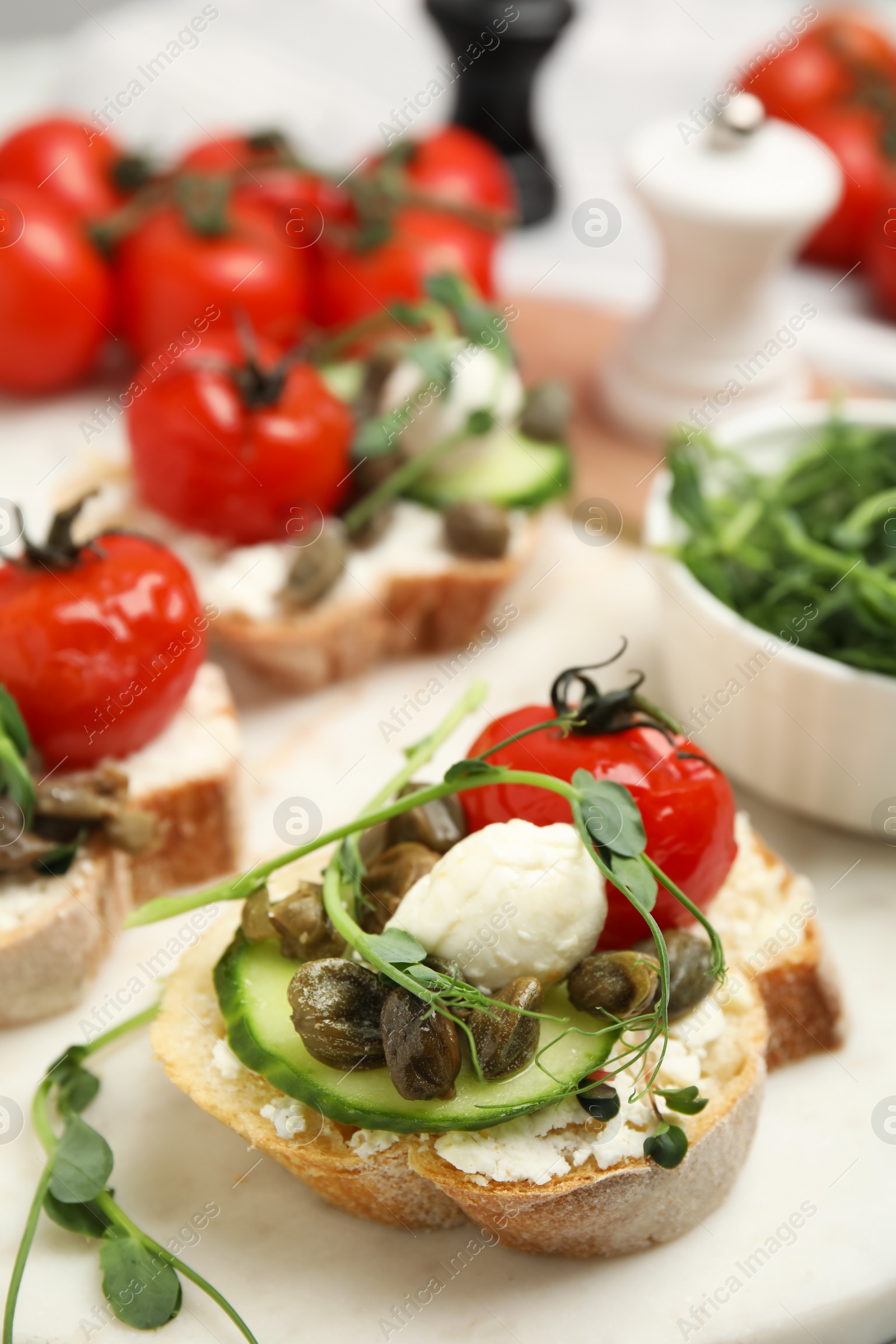 Photo of Tasty bruschettas with capers, vegetables and mozzarella served on white marble board, closeup