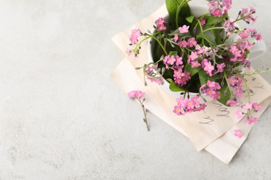 Beautiful pink forget-me-not flowers in cup on light stone table, top view. Space for text