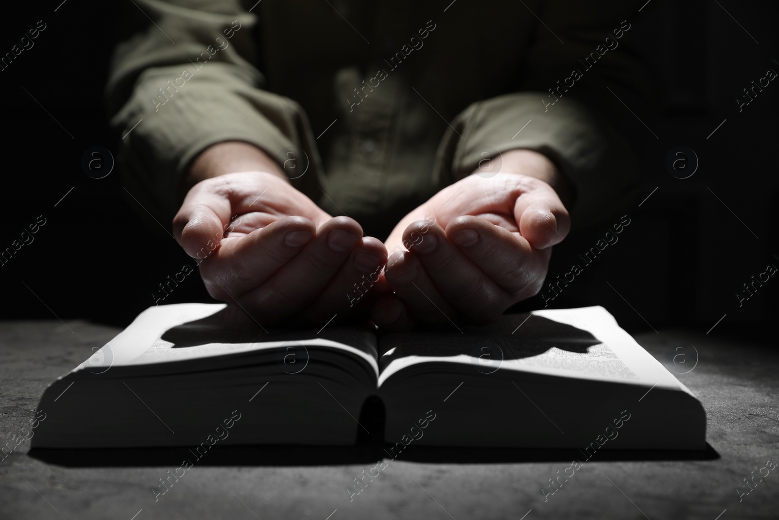 Photo of Religion. Christian man praying over Bible at table, closeup