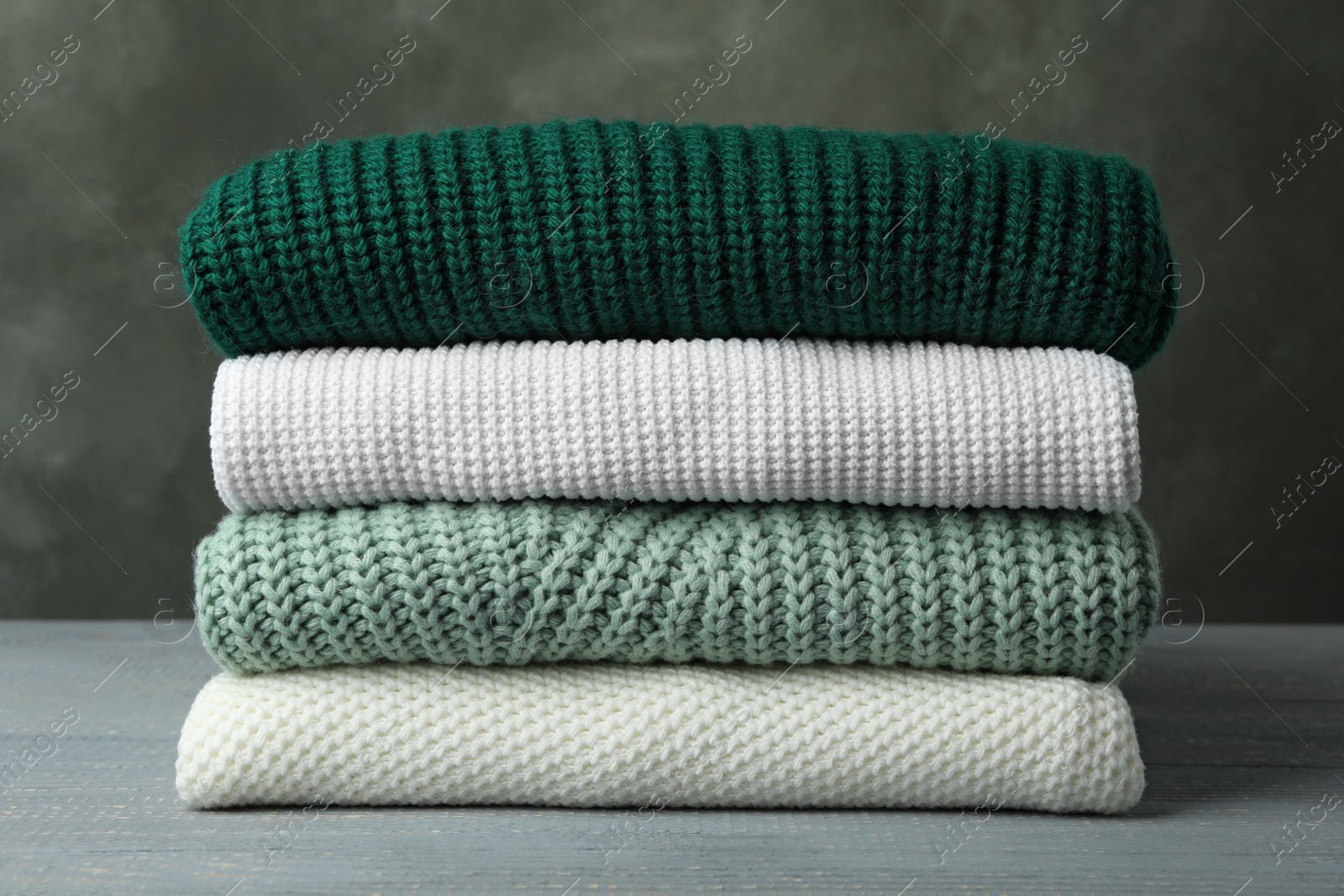 Photo of Stack of warm clothes on wooden table against grey background. Autumn season