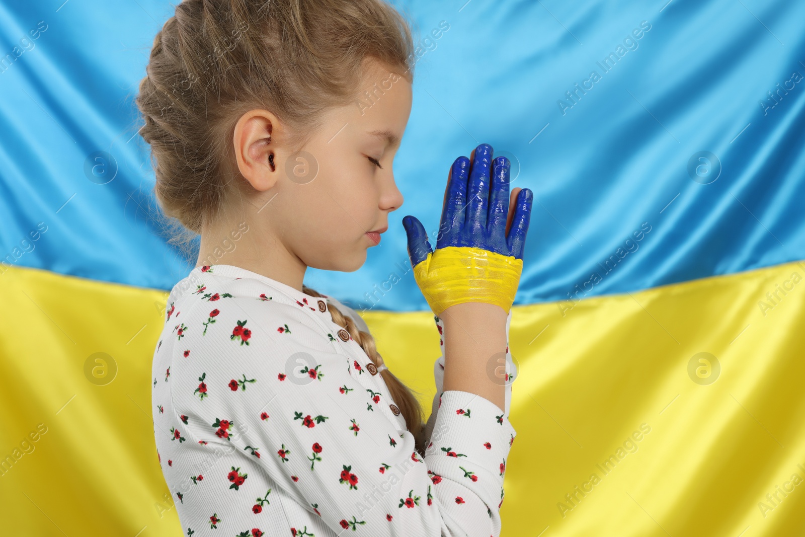 Photo of Little girl with clasped painted hands near Ukrainian flag