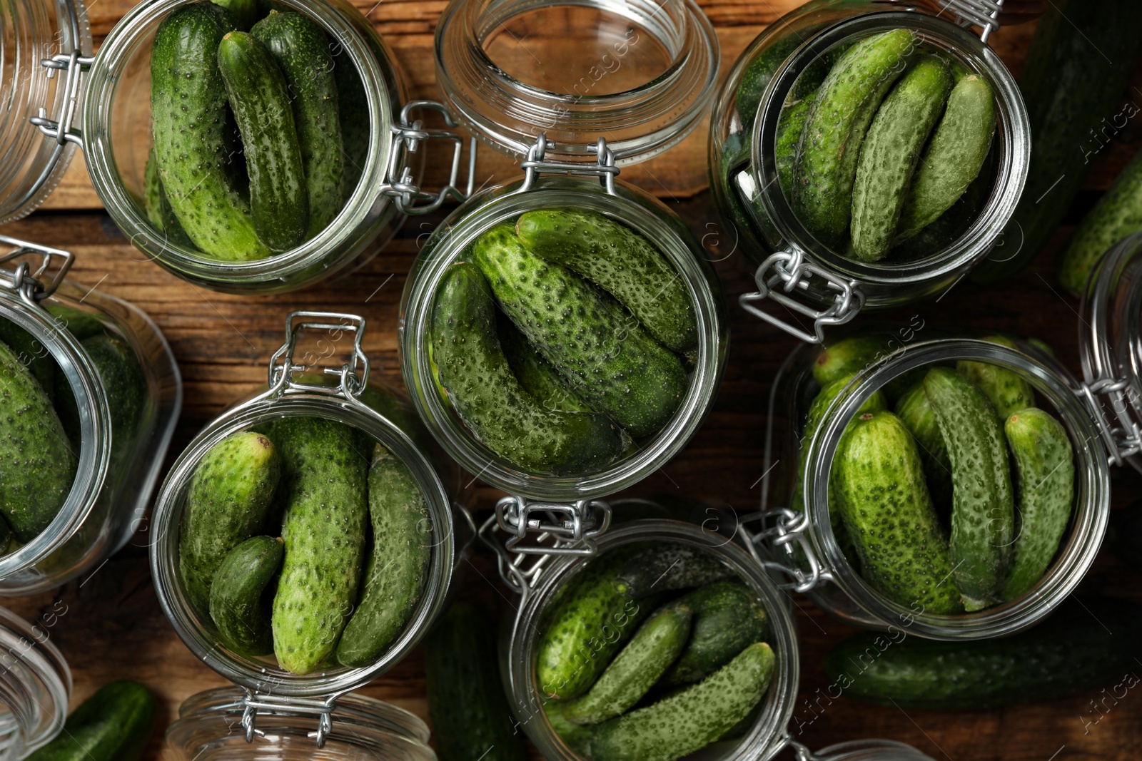 Photo of Pickling jars with fresh cucumbers on wooden table, flat lay