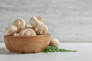 Bowl with fresh champignon mushrooms on wooden table, space for text