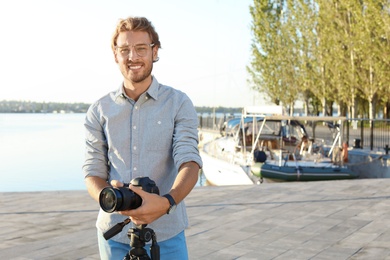 Young male photographer standing with professional camera at pier. Space for text