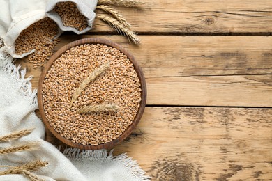 Photo of Bowl of wheat grains and spikes on wooden table, flat lay. Space for text