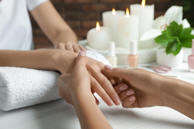 Photo of Cosmetologist massaging client's hand at table in spa salon, closeup