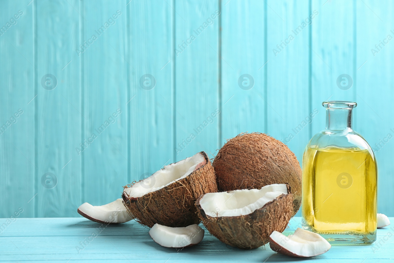 Photo of Bottle of natural organic oil and coconuts on blue wooden table. Space for text