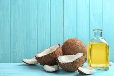 Bottle of natural organic oil and coconuts on blue wooden table. Space for text