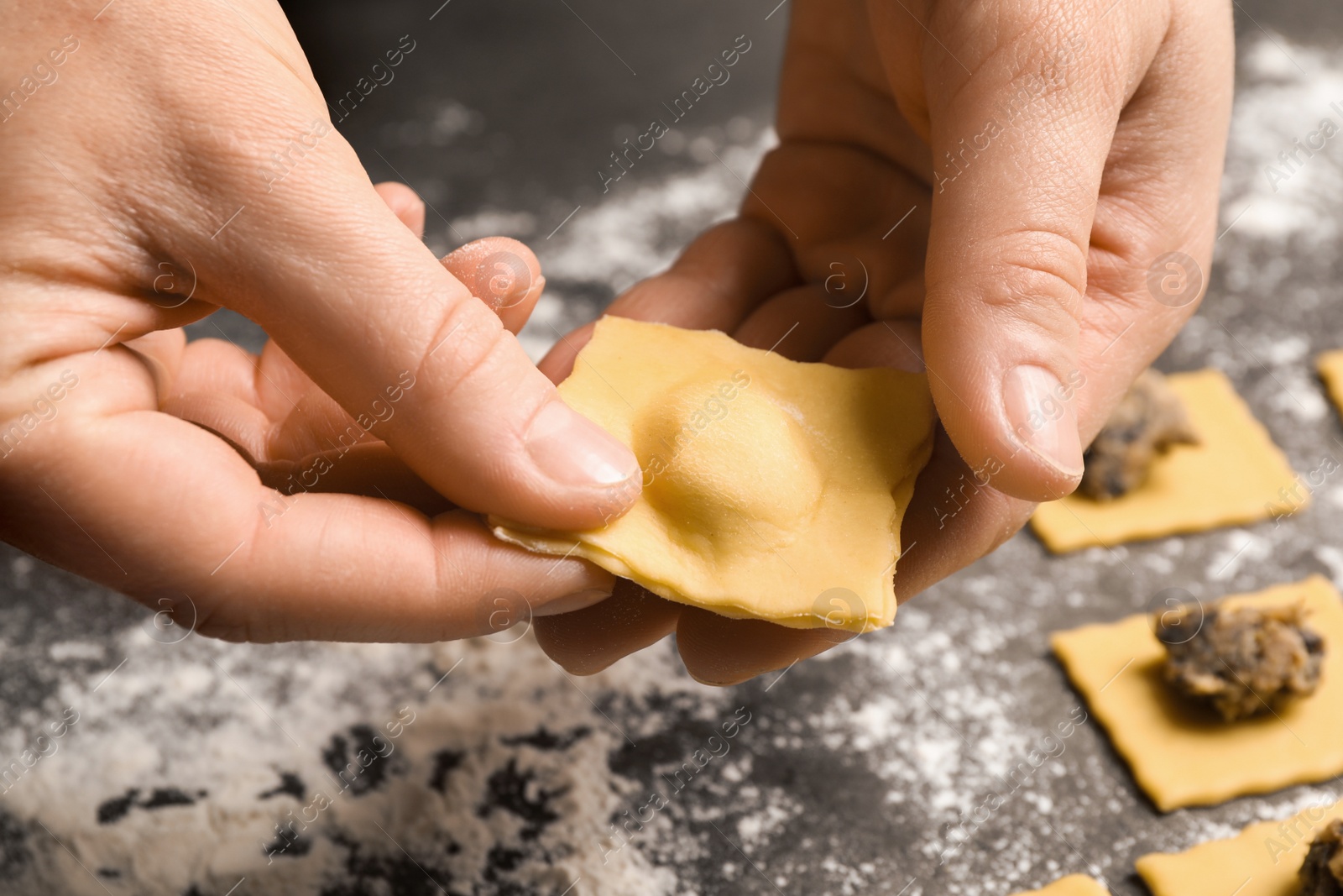 Photo of Woman making ravioli at grey table, closeup. Italian pasta