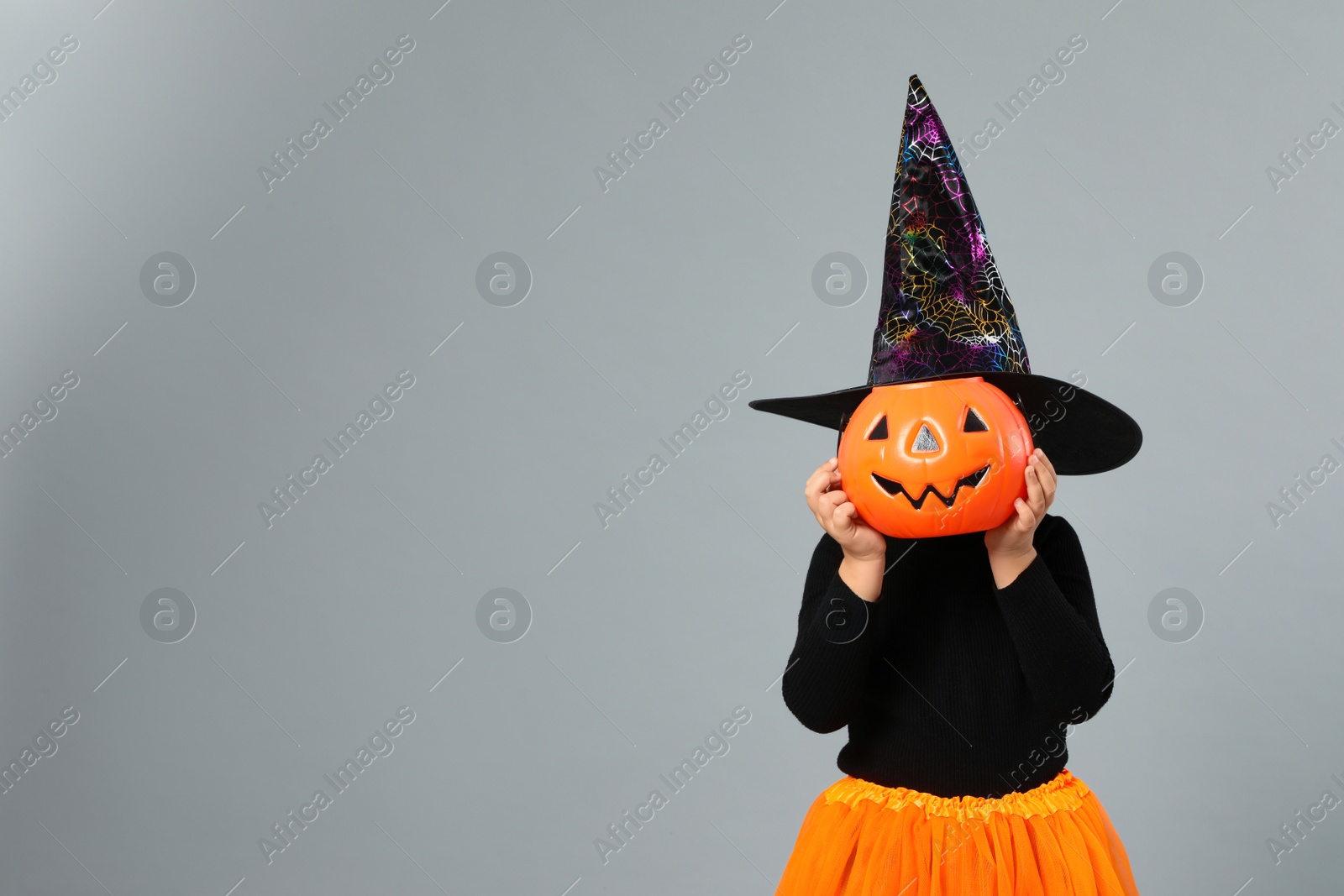 Photo of Cute little girl with pumpkin candy bucket wearing Halloween costume on grey background, space for text