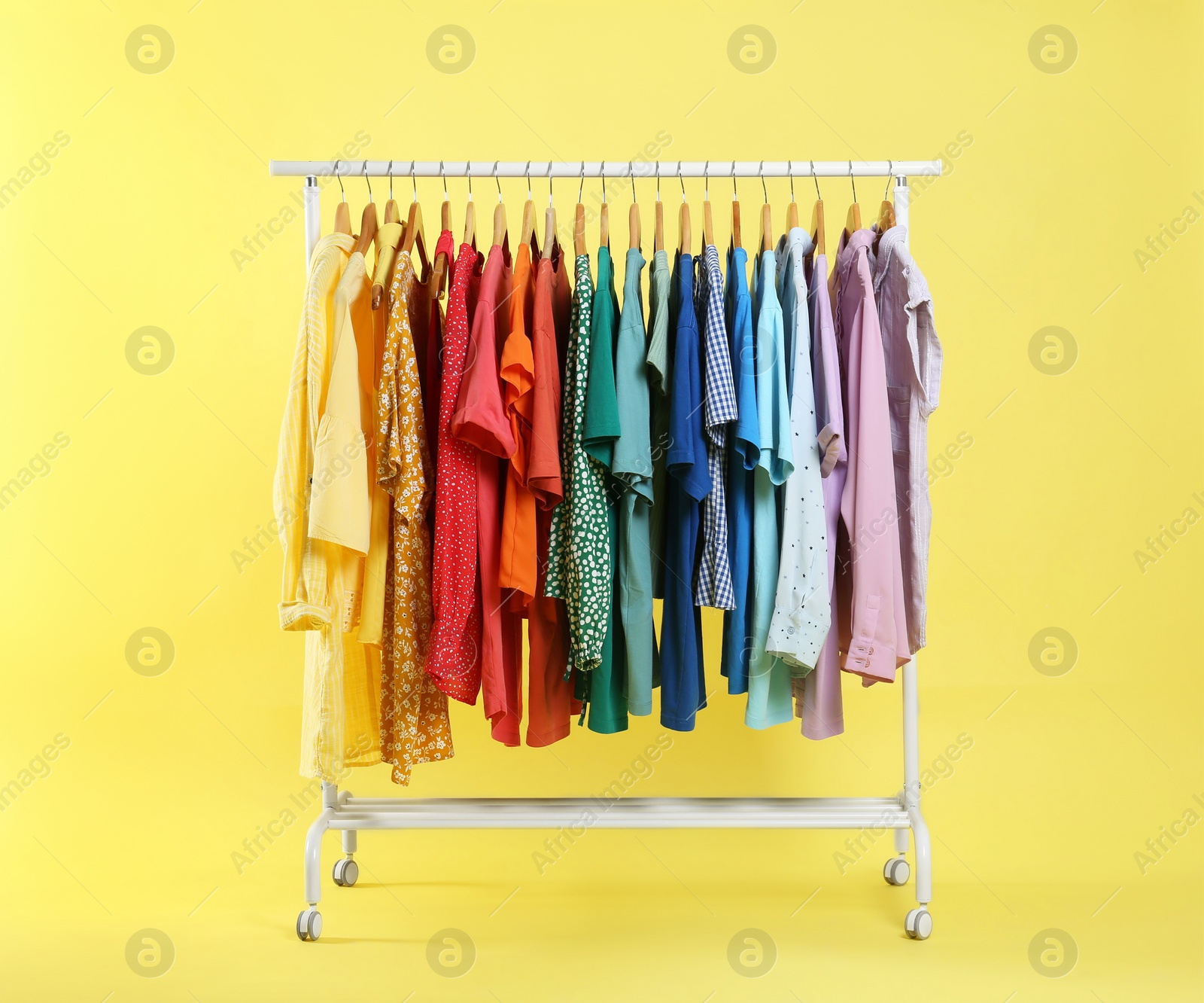 Photo of Bright clothes hanging on rack against yellow background. Rainbow colors