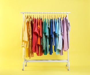 Photo of Bright clothes hanging on rack against yellow background. Rainbow colors