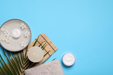 Flat lay composition with spa products, burning candle and beautiful flowers on light blue background. Space for text