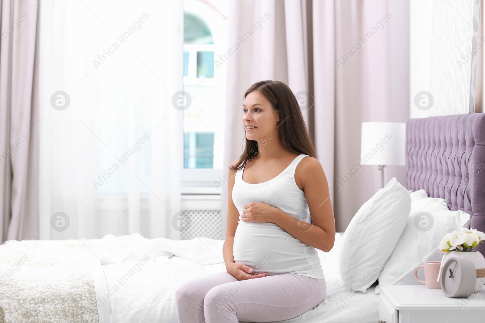 Photo of Happy pregnant woman sitting on bed at home