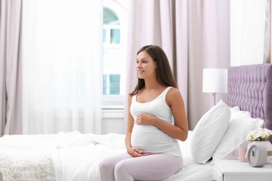 Happy pregnant woman sitting on bed at home