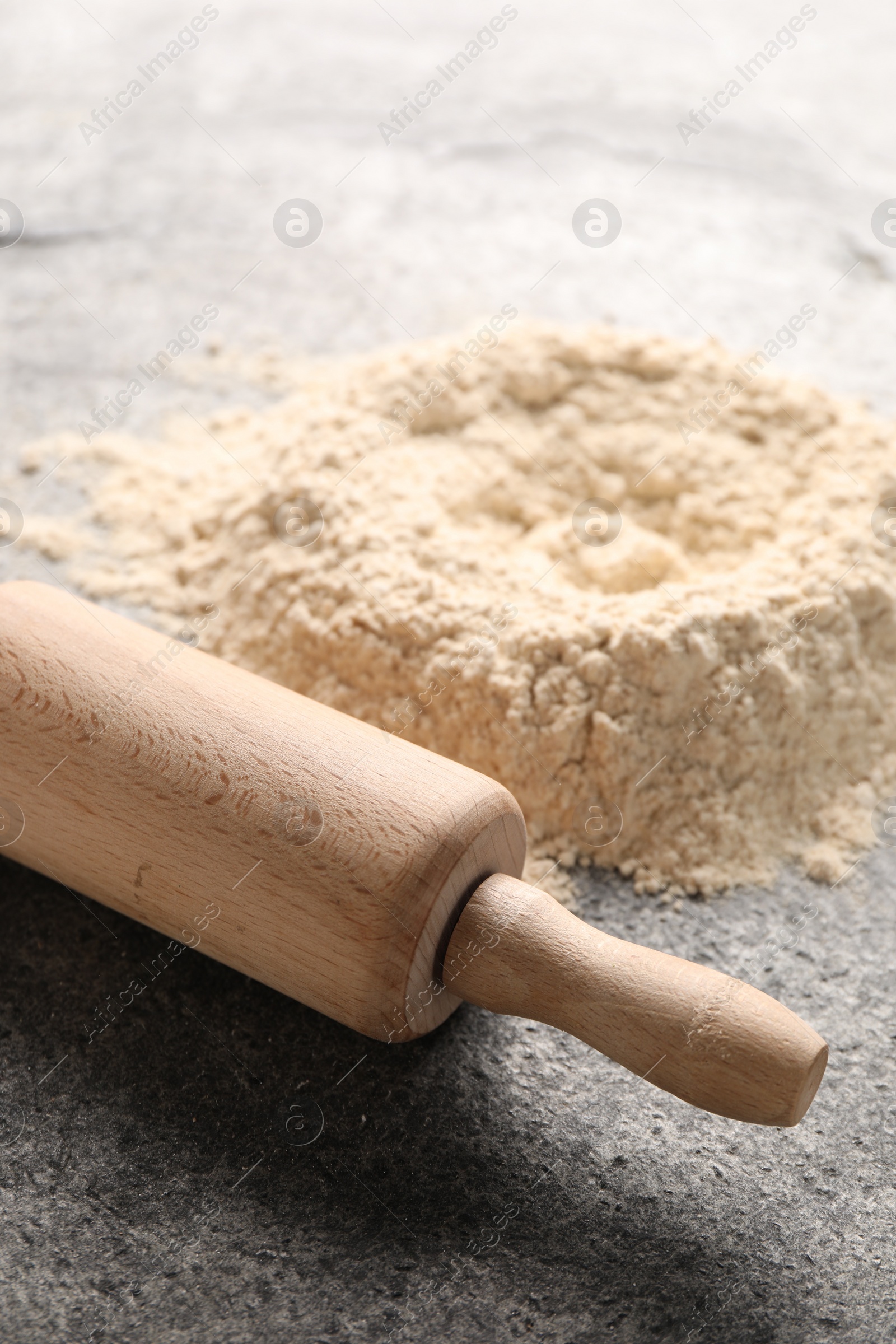 Photo of Rolling pin and scattered flour on grey textured table, closeup