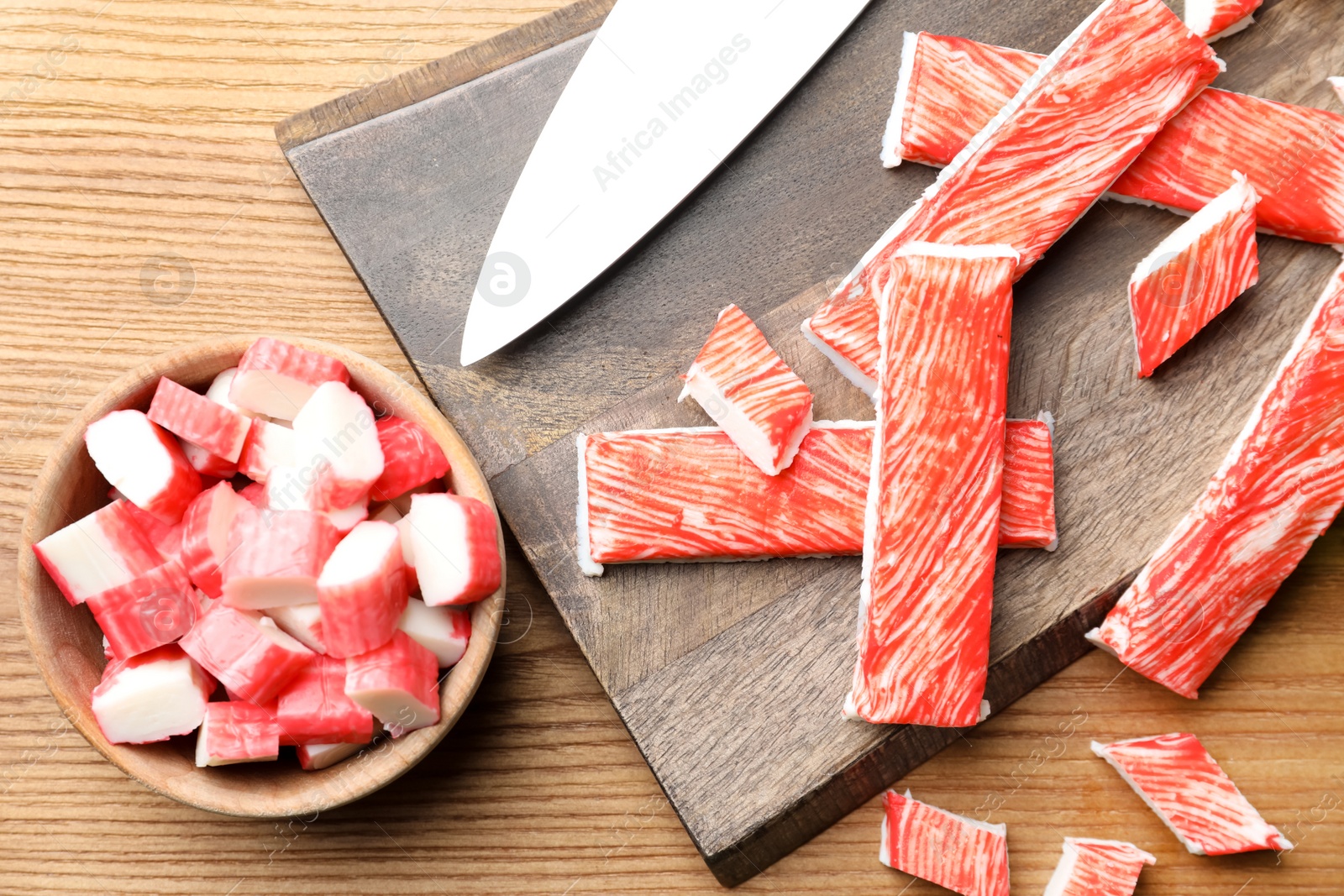 Photo of Delicious crab sticks with knife on wooden table, flat lay