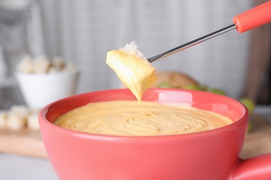 Dipping bread into pot with cheese fondue, closeup