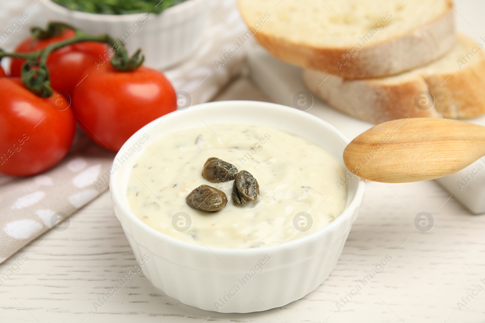 Photo of Creamy caper sauce in bowl on white wooden table, closeup