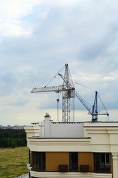 Photo of Construction site with tower cranes near modern building under cloudy sky
