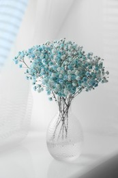 Photo of Beautiful dyed gypsophila flowers in glass vase on white table