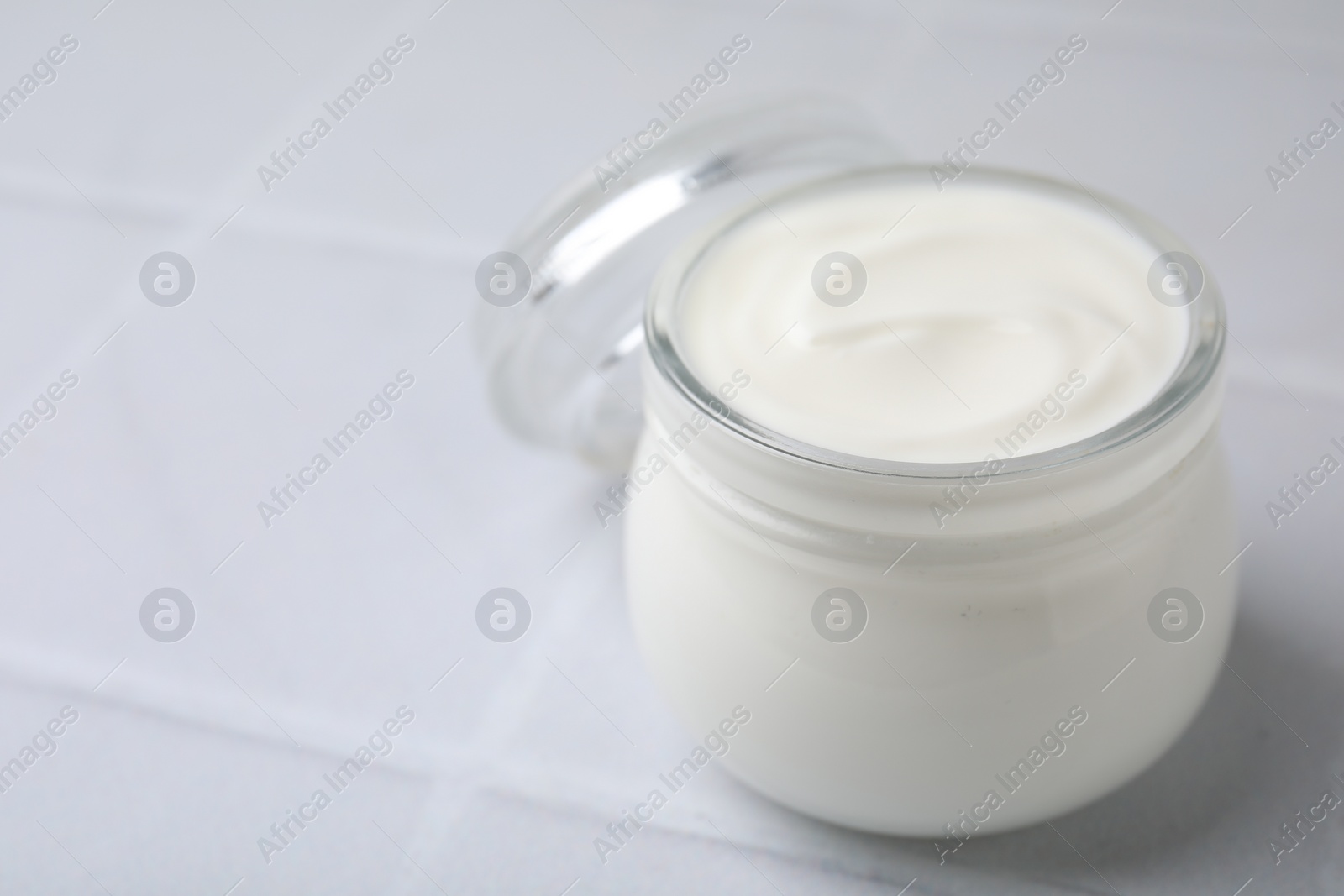 Photo of Delicious natural yogurt in glass jar on white tiled table, closeup. Space for text