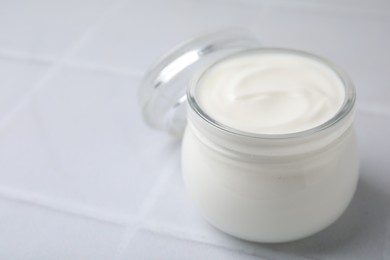 Delicious natural yogurt in glass jar on white tiled table, closeup. Space for text