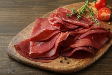 Photo of Tasty bresaola, peppercorns, tomatoes and thyme on wooden table, closeup