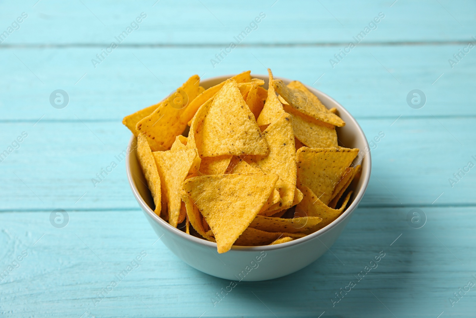 Photo of Tasty mexican nachos chips in bowl on blue wooden table