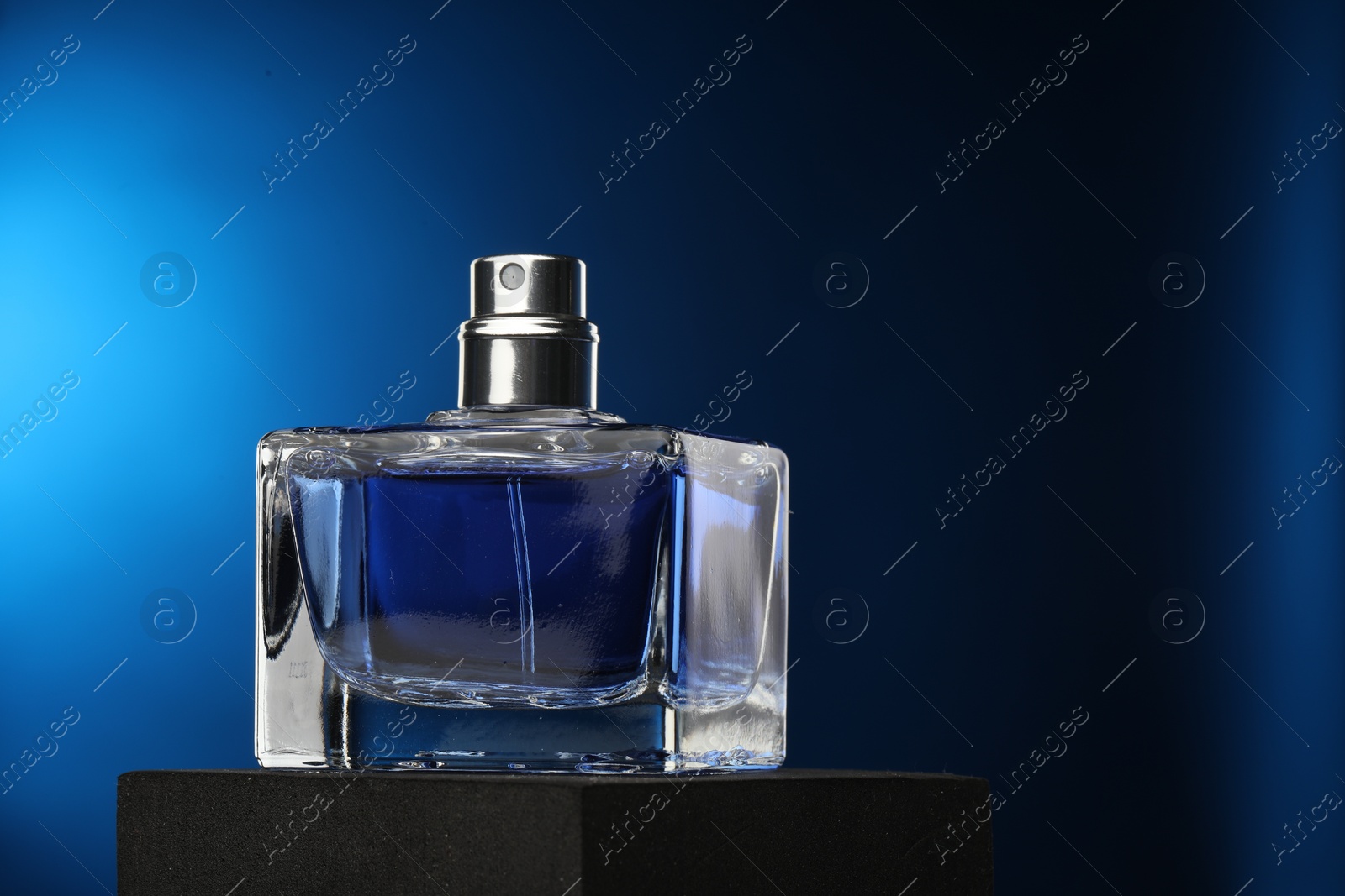 Photo of Luxury men`s perfume in bottle against dark blue background, space for text