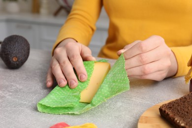 Photo of Woman packing piece of cheese into beeswax food wrap at light table in kitchen, closeup