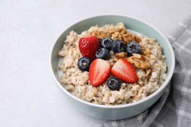 Photo of Tasty oatmeal with strawberries, blueberries and walnuts in bowl on grey table