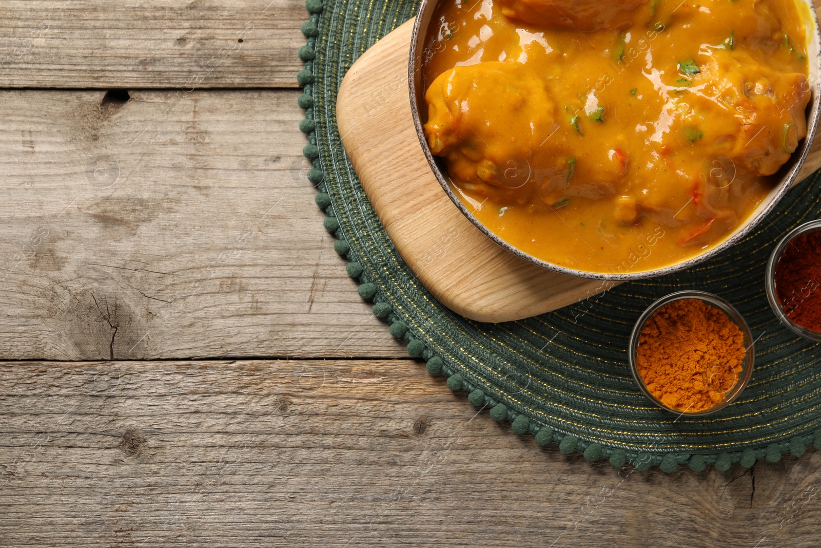 Photo of Tasty chicken curry and spices on wooden table, top view. Space for text