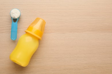 Photo of Feeding bottle with infant formula and powder on wooden table, flat lay. Space for text