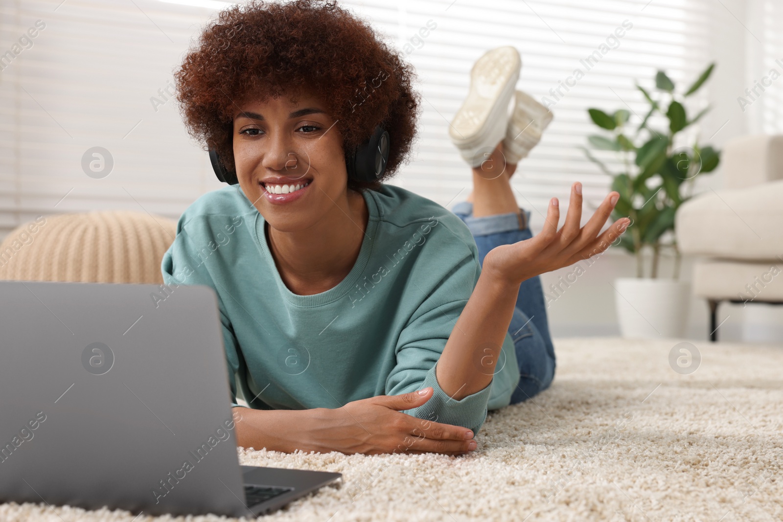 Photo of Beautiful young woman in headphones having video chat via laptop in room