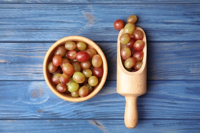 Photo of Scoop and bowl with fresh ripe juicy grapes on wooden background, top view